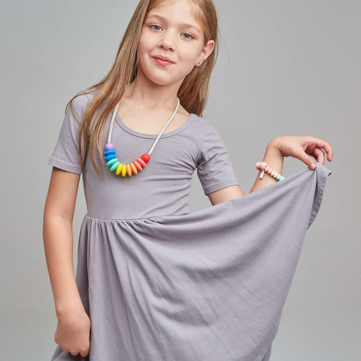 Young girl wearing a gray dress with a colorful necklace against a gray background