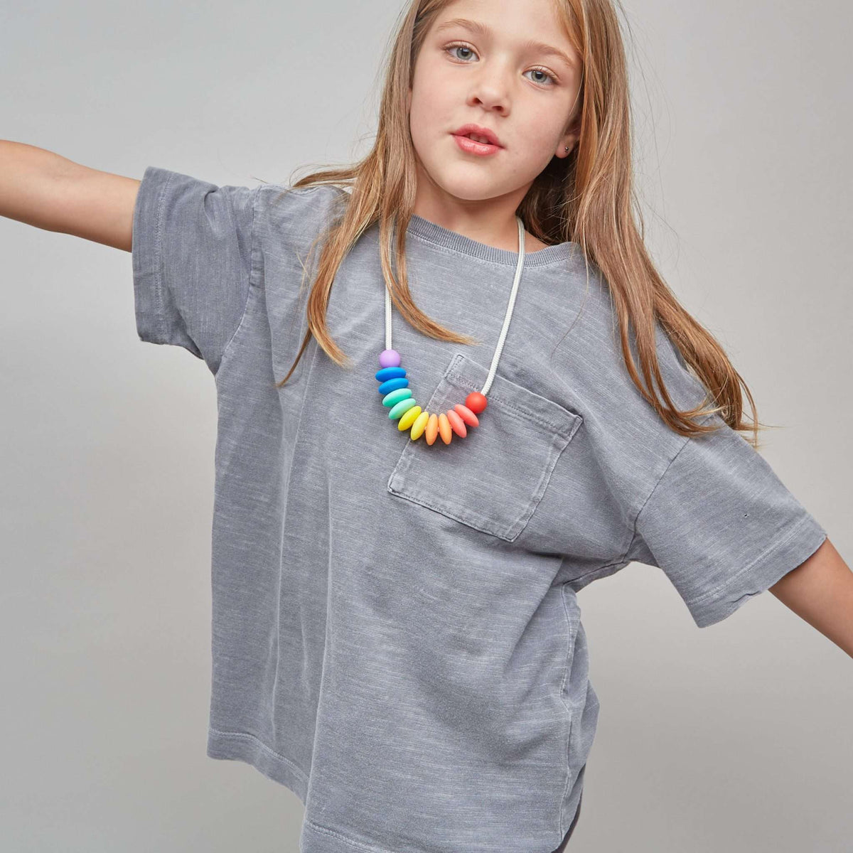 Young girl wearing a gray oversized t-shirt and colorful necklace on a plain background