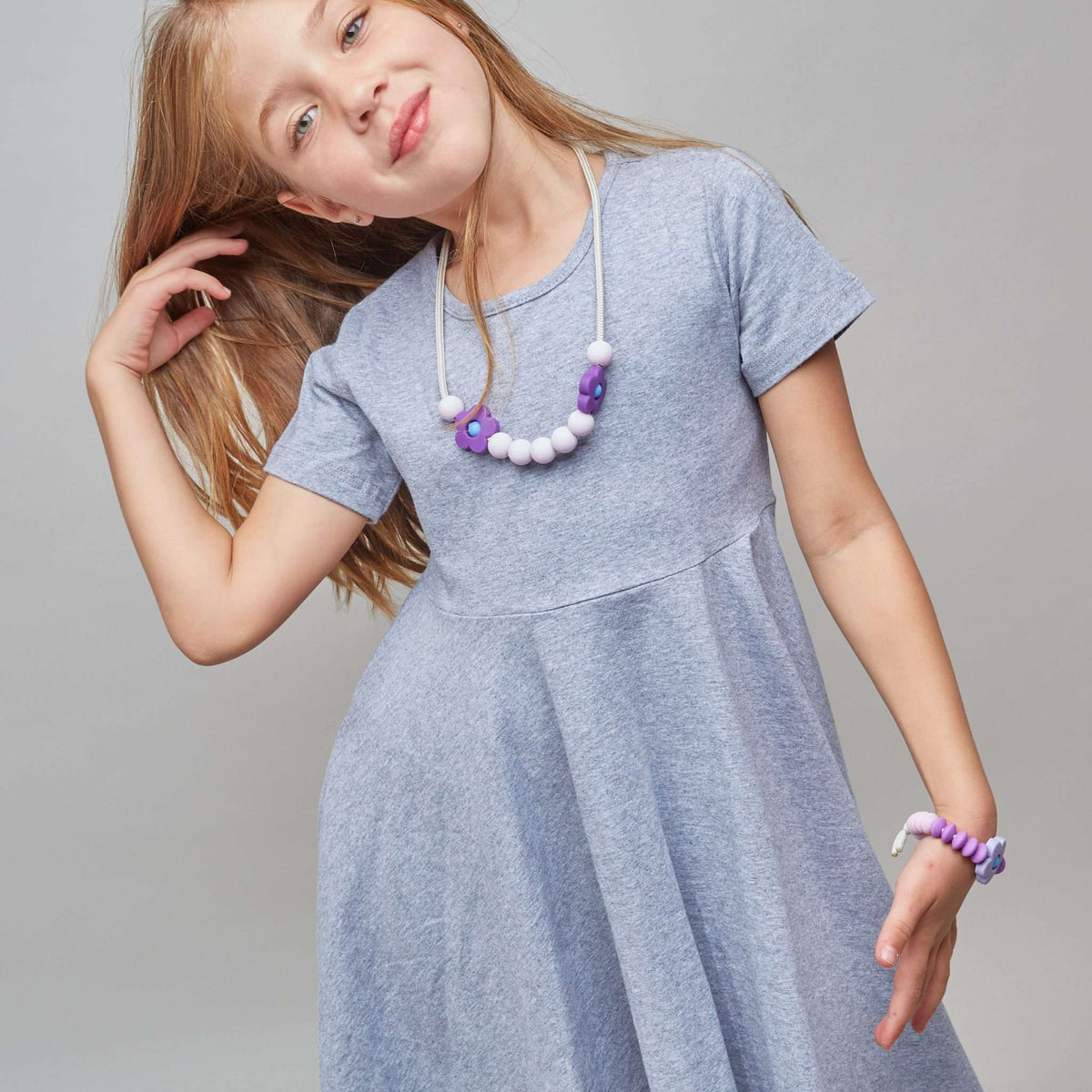 Young girl wearing a gray dress with a necklace on a plain background