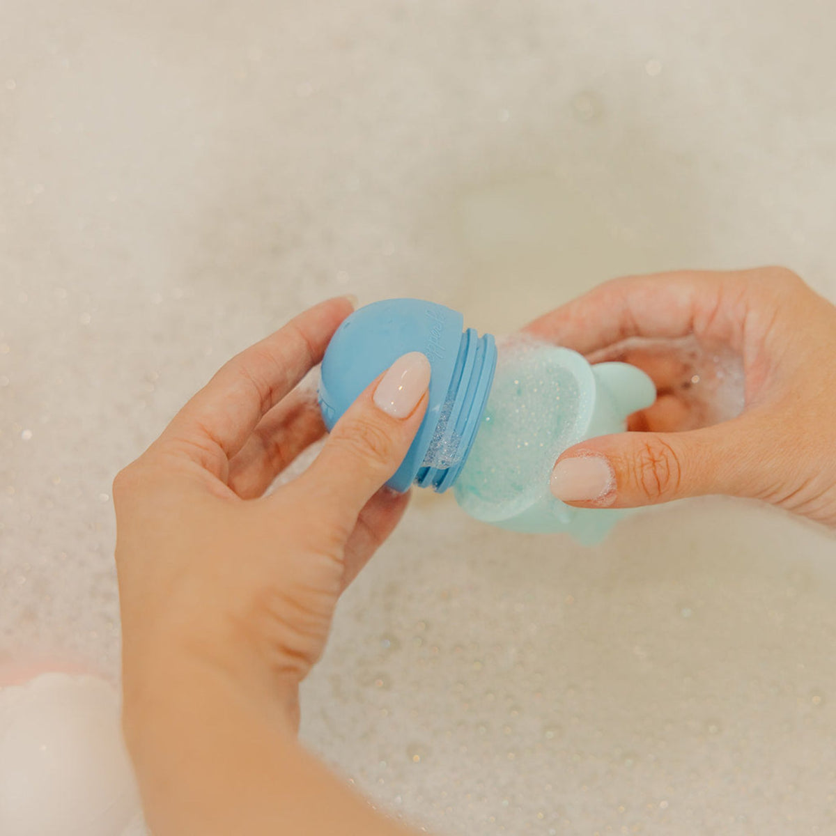 Person holding a blue and clear bath bomb in water with bubbles
