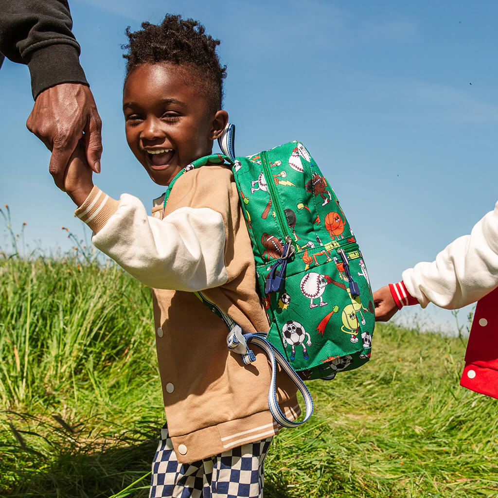 Child with a colorful backpack being held by an adult in a grassy field