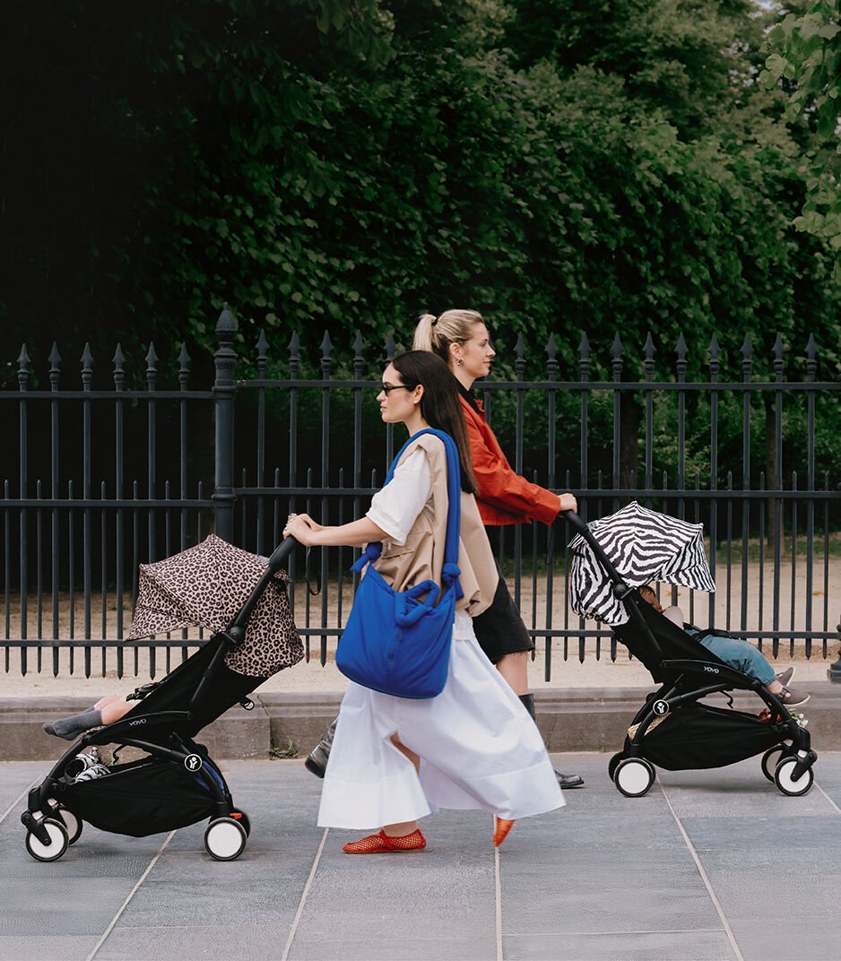 Two women walking with strollers in an urban setting