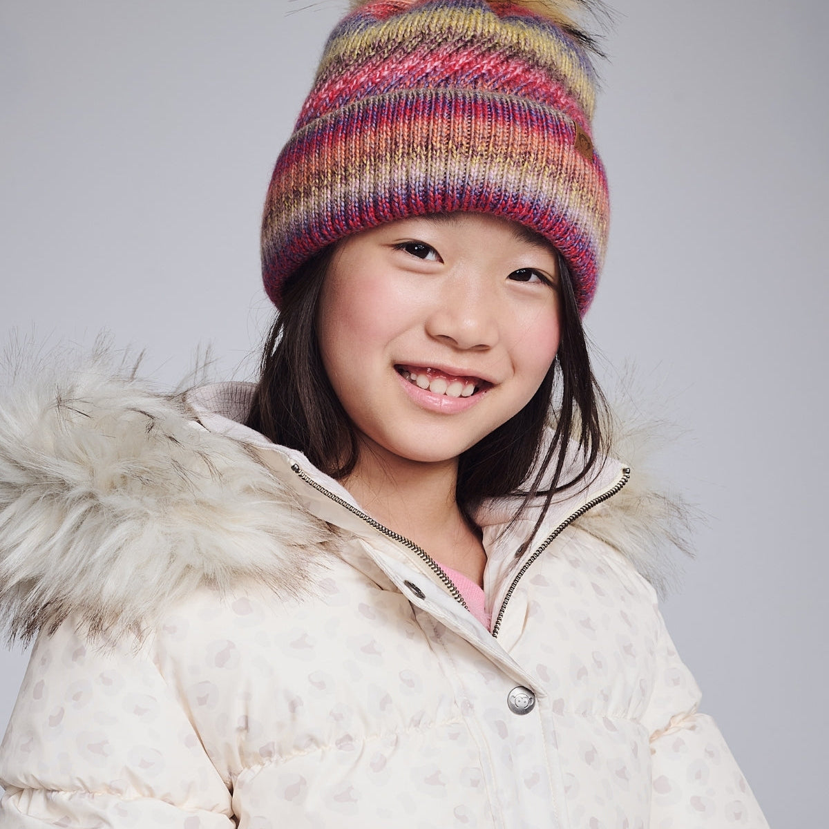 Child wearing a colorful striped beanie and white winter coat on a plain background