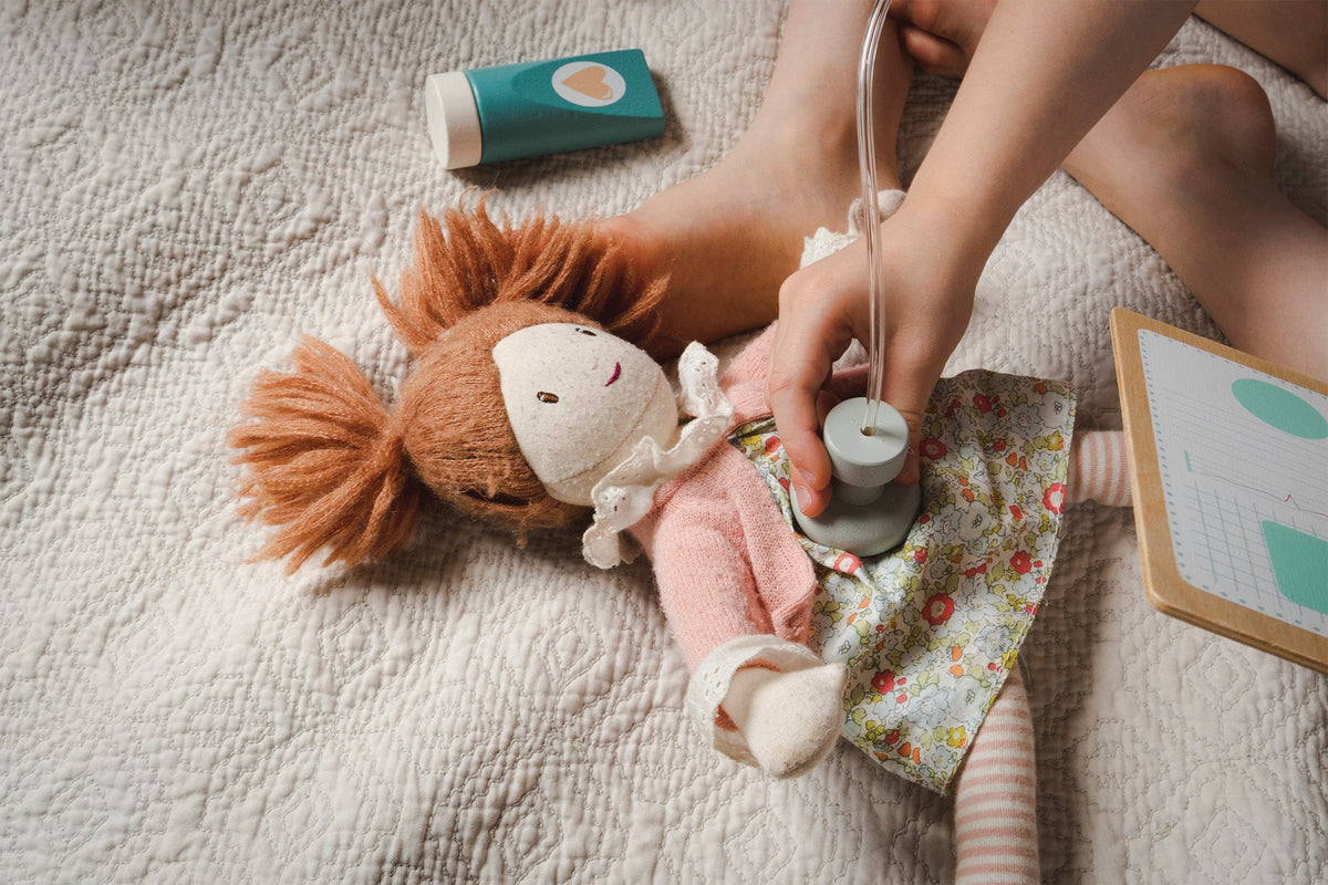 Child playing with a doll and stethoscope on a bed