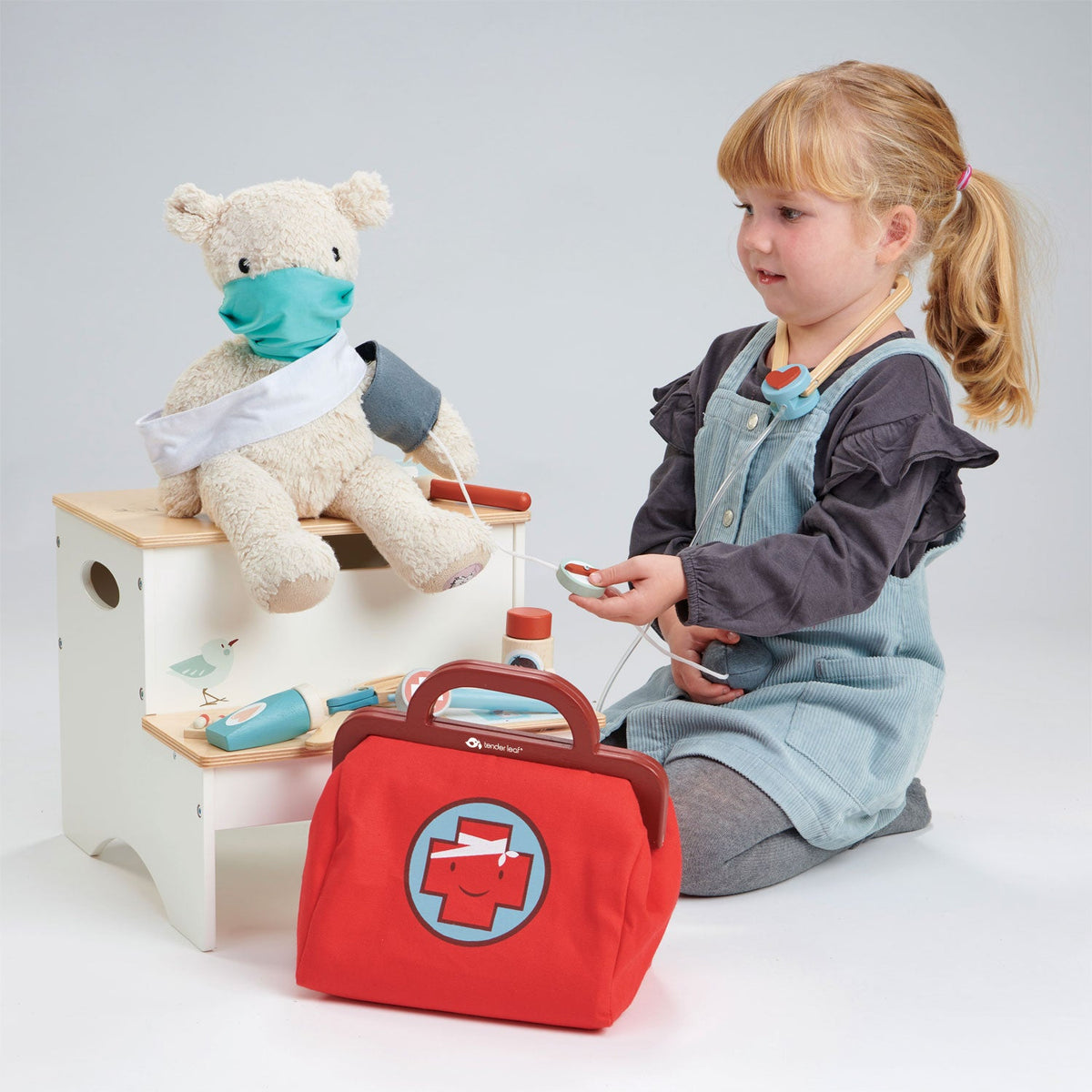 Child playing with a toy medical kit and teddy bear on a white background