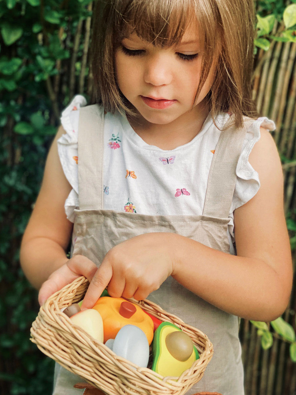 Child holding a basket with toy fruits and vegetables outdoors