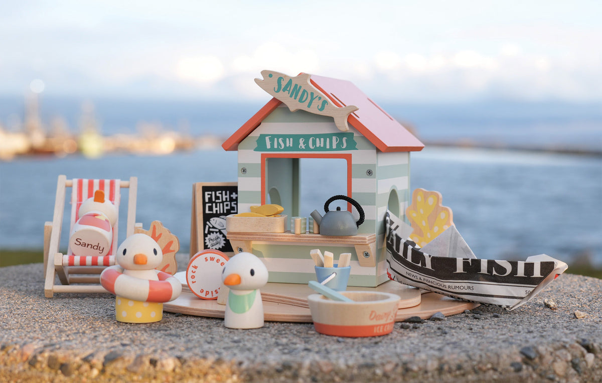 Toy set with a beach hut, boat, and seagulls on a stone surface with water in the background
