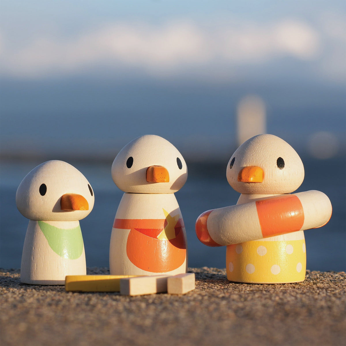 Three wooden duck toys on a beach with a blurred ocean background