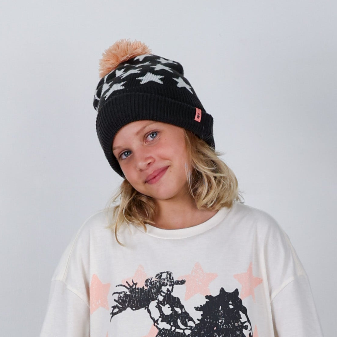 Person wearing a black beanie with white patterns and a pink pom-pom, and a white sweater with black and pink designs.