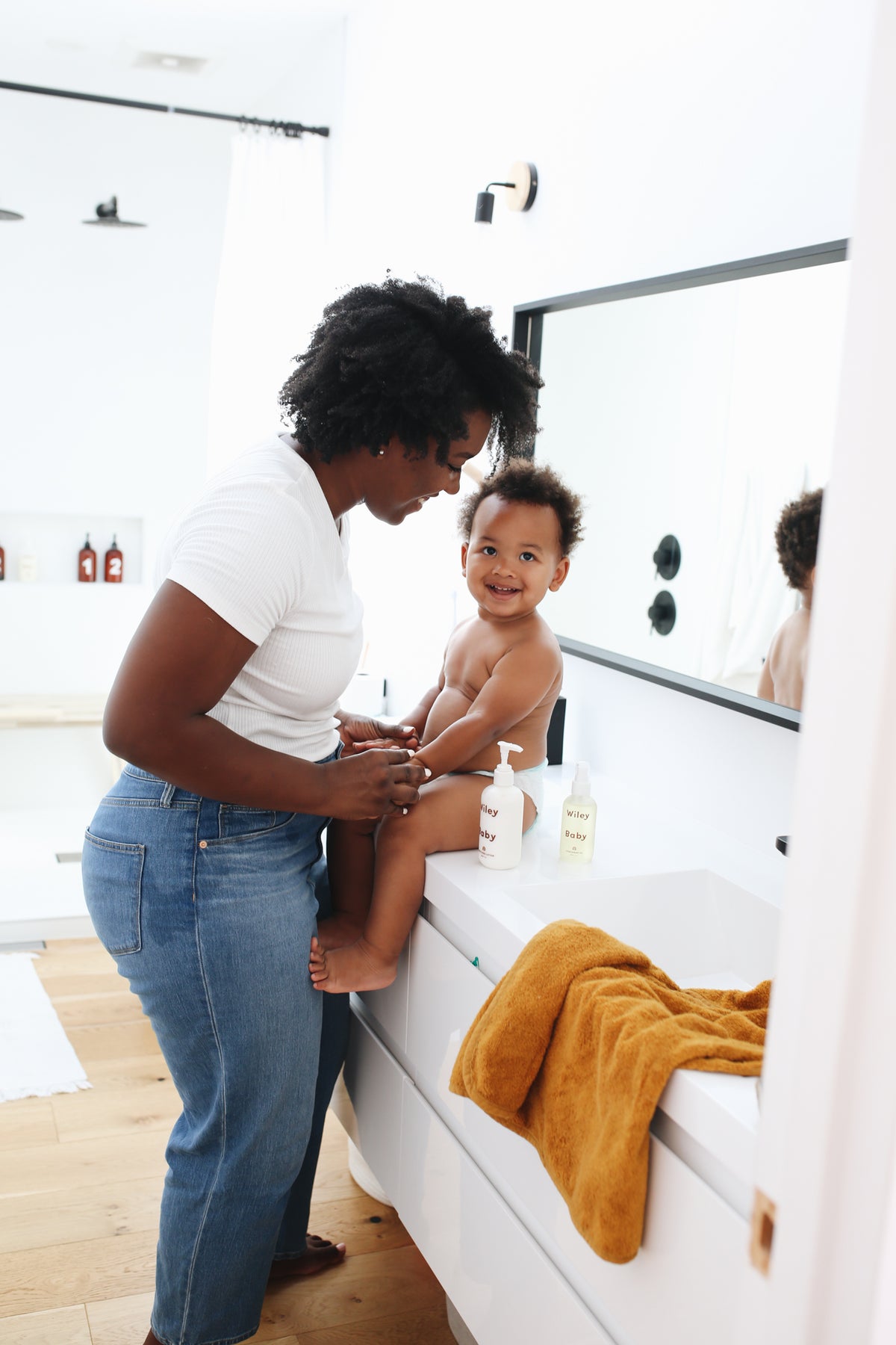 Woman and child in a bathroom with a yellow towel on a white bathtub.