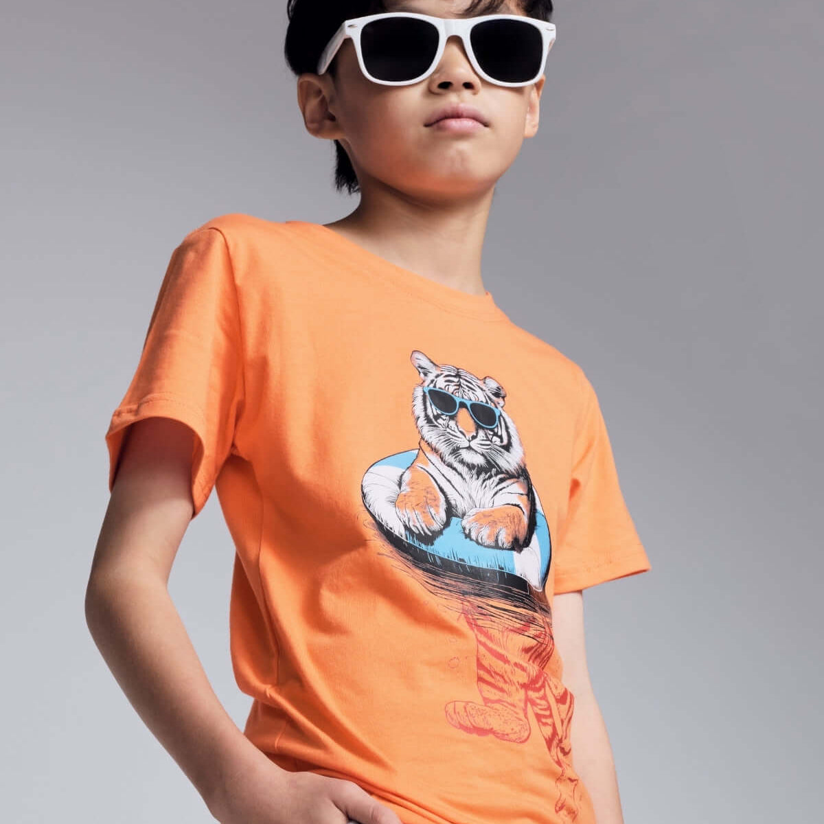 Child wearing an orange t-shirt with a tiger graphic and sunglasses on a gray background