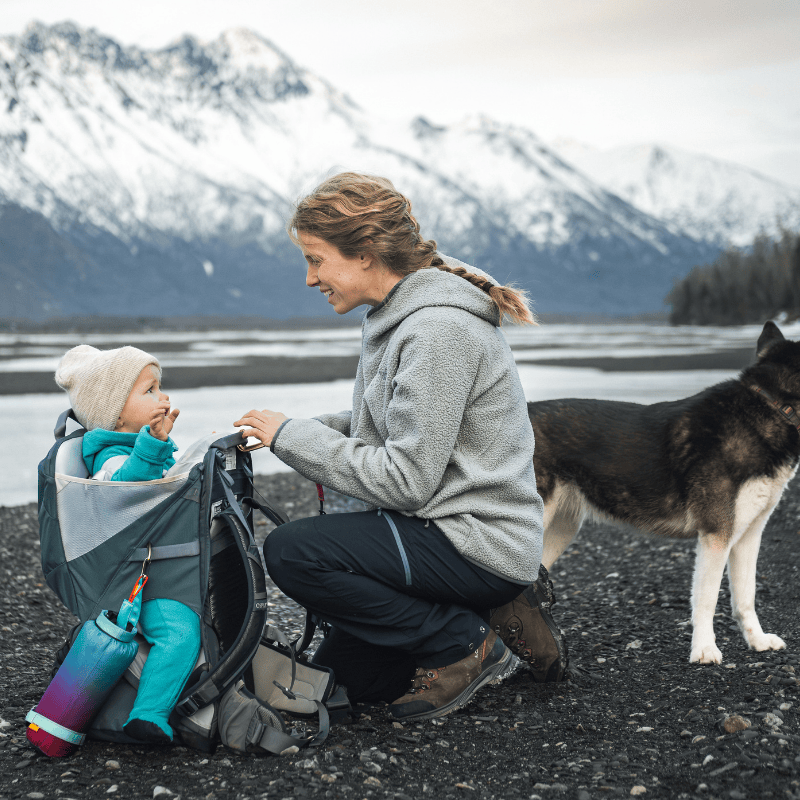 Woman and child with a dog by a lake with mountains in the background