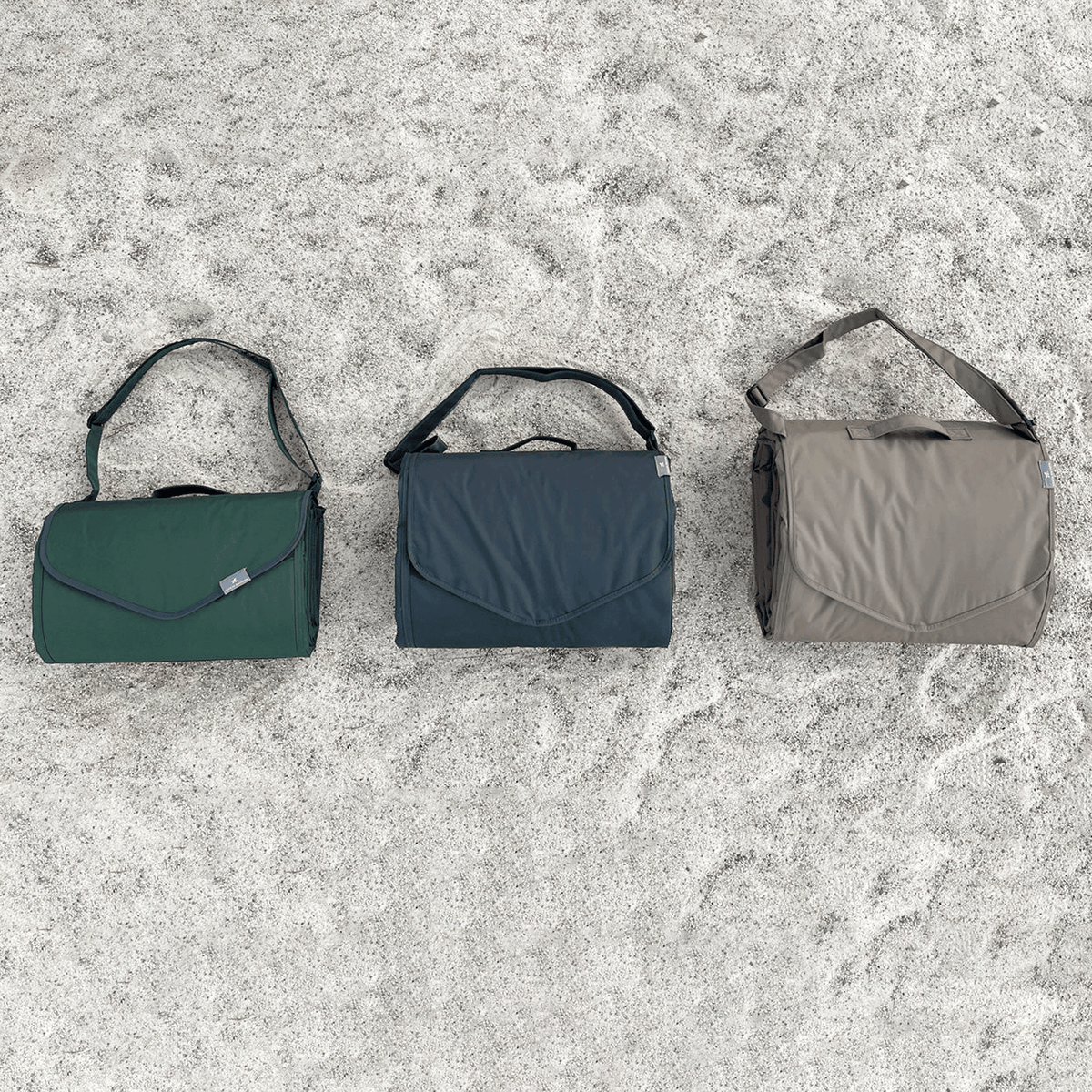 Three messenger bags in green, blue, and gray on a textured surface