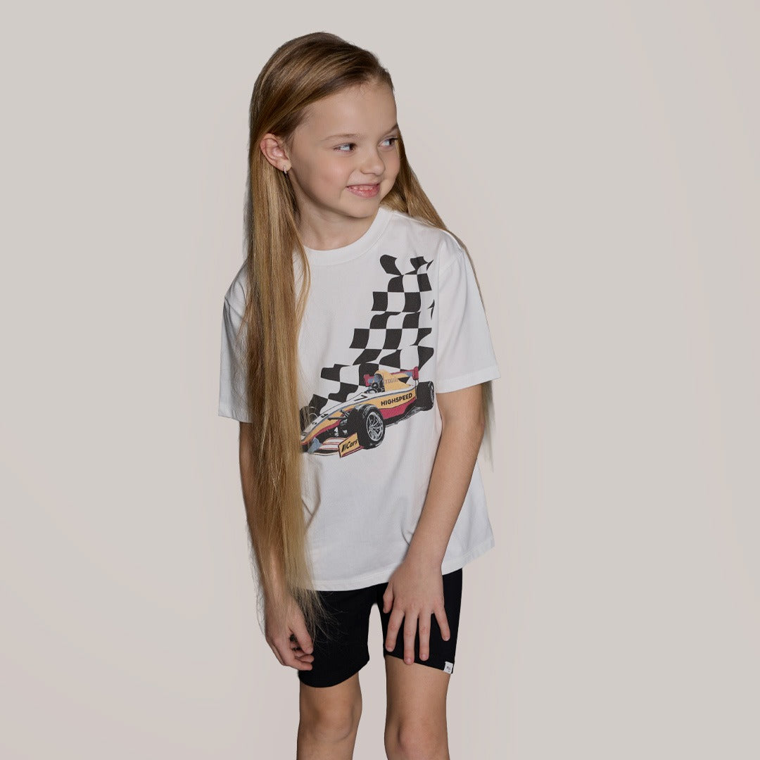 Young girl wearing a white t-shirt with a car and checkered flag design on a plain background