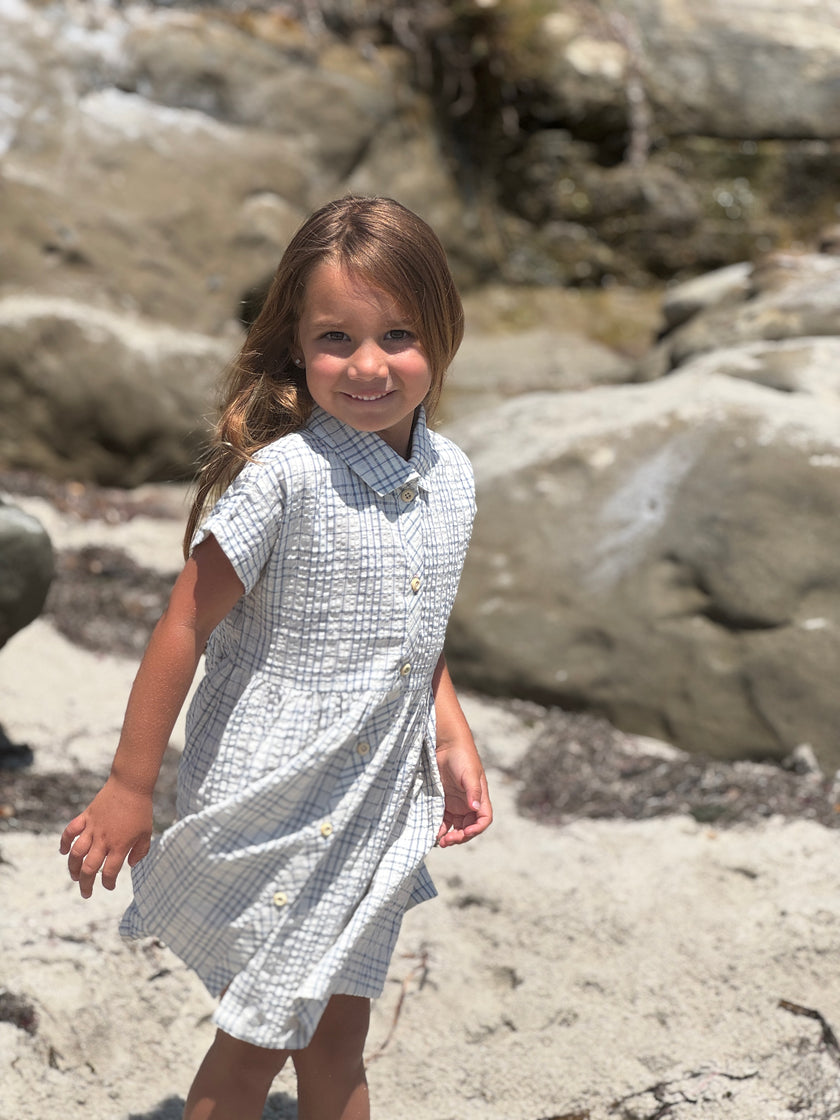 Young girl in a blue dress standing on a rocky beach