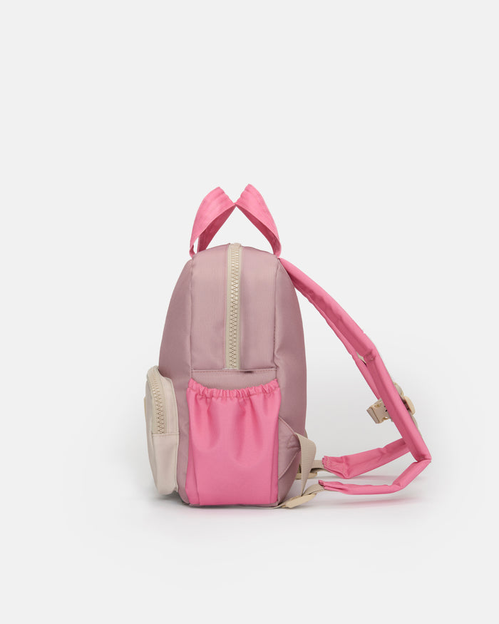 A small pink backpack with a front zippered pocket and matching pink shoulder straps, shown against a plain light gray studio background.