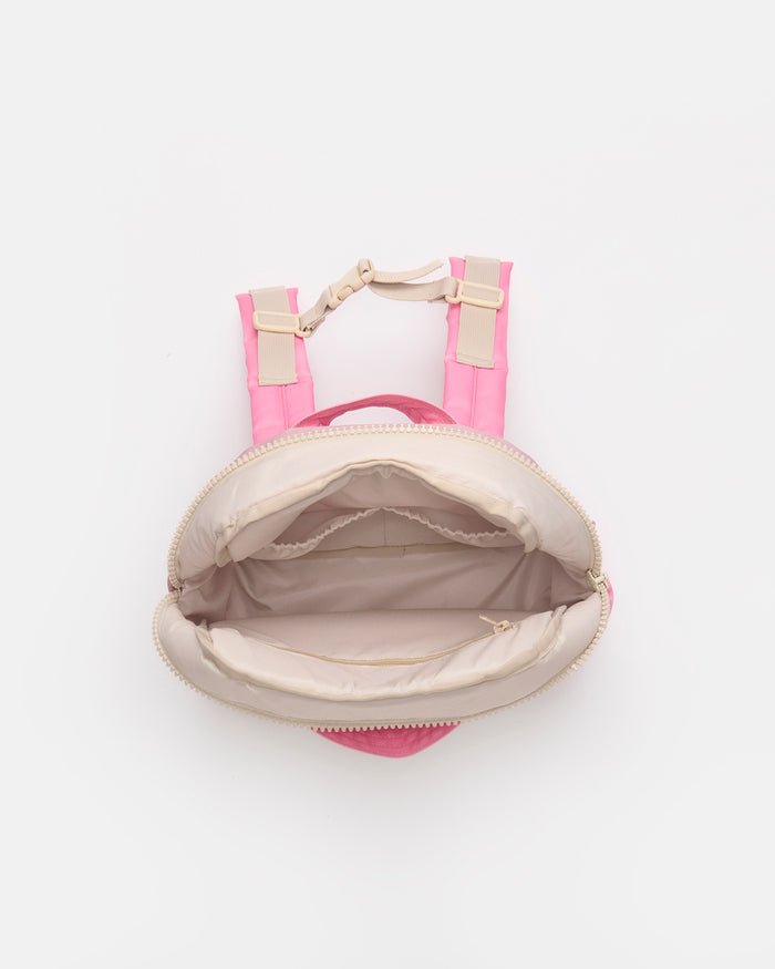 A small pink backpack shown from a top-down view, open to reveal a beige interior lining and light beige shoulder straps with gold-tone hardware, on a plain white background.
