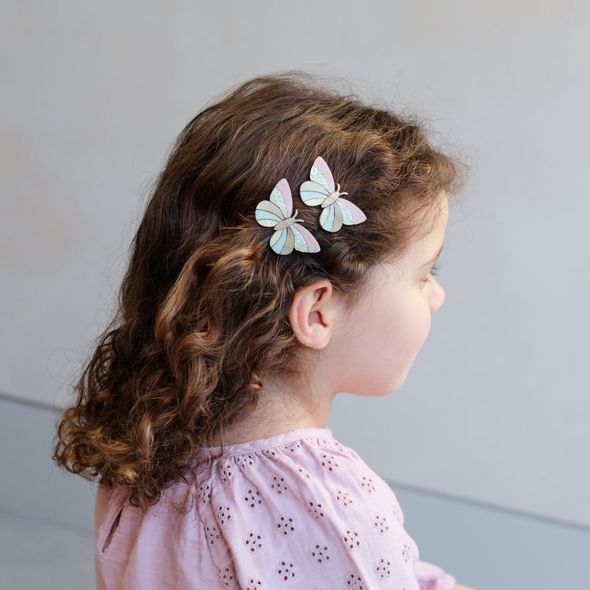 Child with butterfly hair clips on a plain background