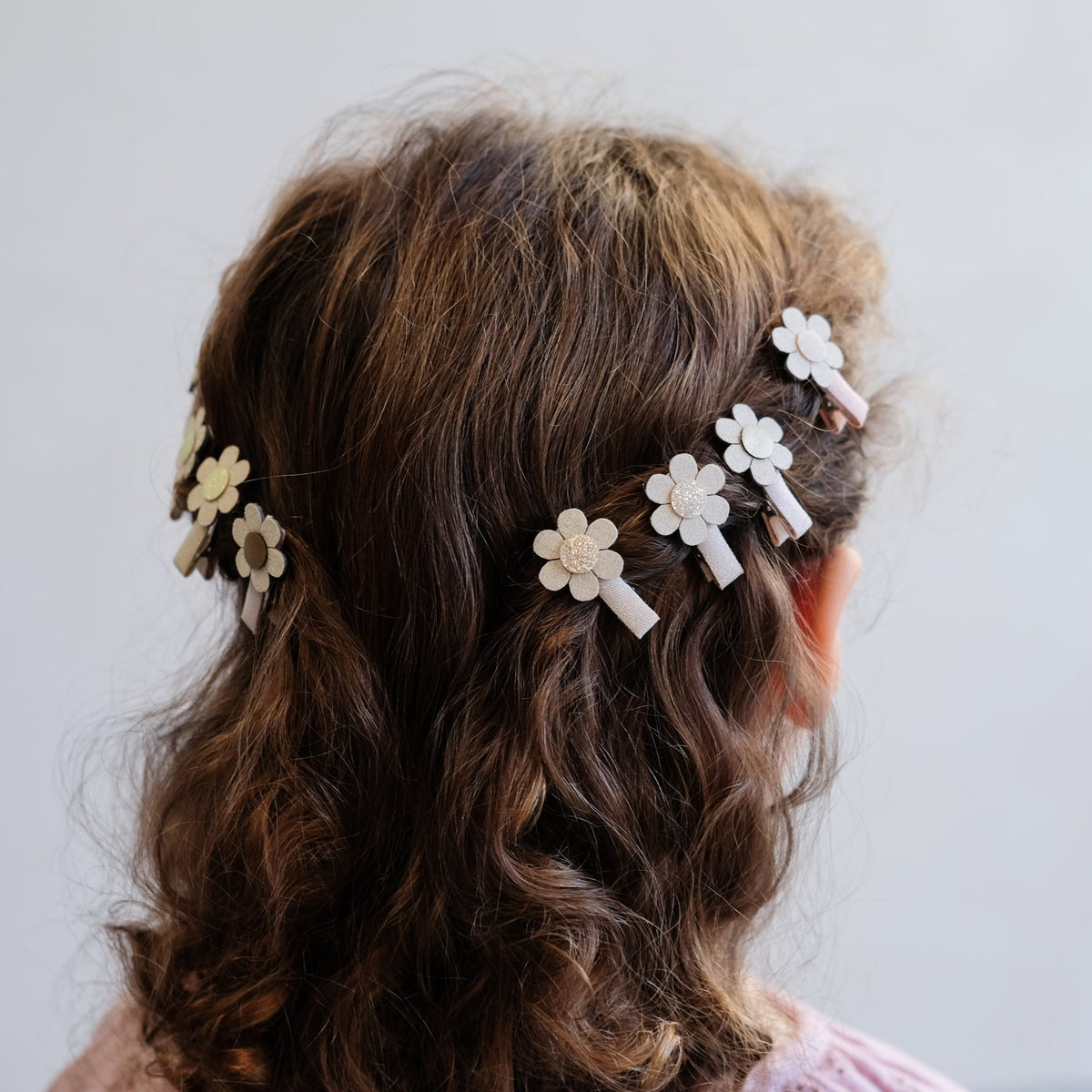 Woman with wavy hair wearing floral hair clips against a plain background