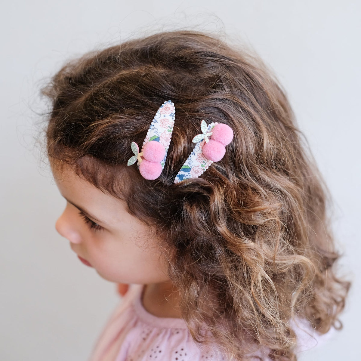 Child with floral hair clip and pink hair tie on a plain background
