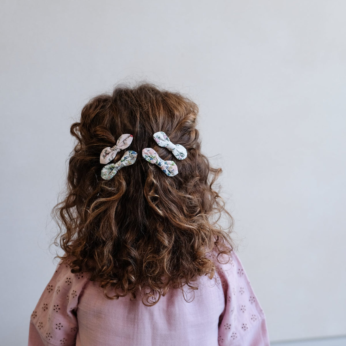Person with curly hair wearing a floral hair clip against a plain background