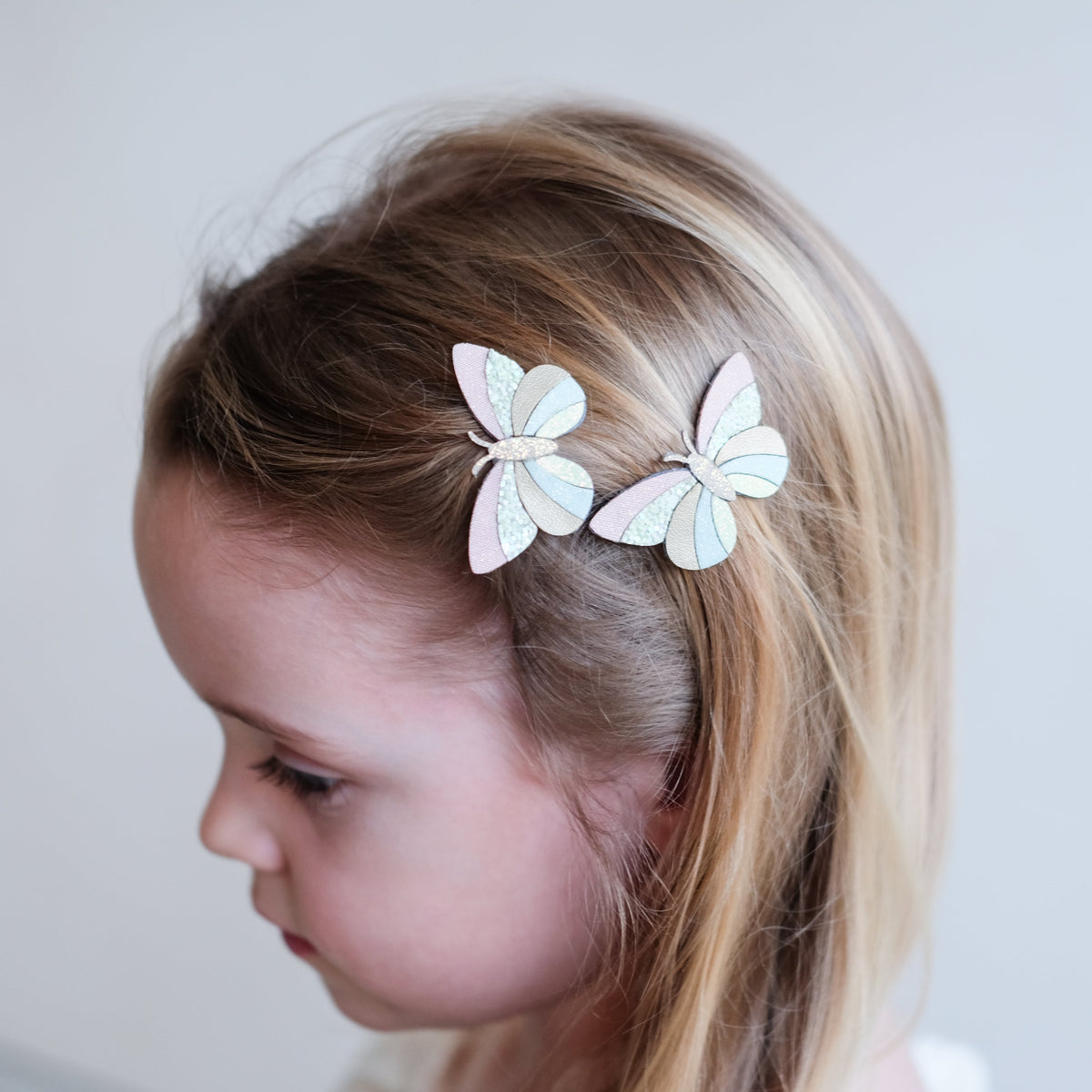 Child with butterfly hair clips on a plain background
