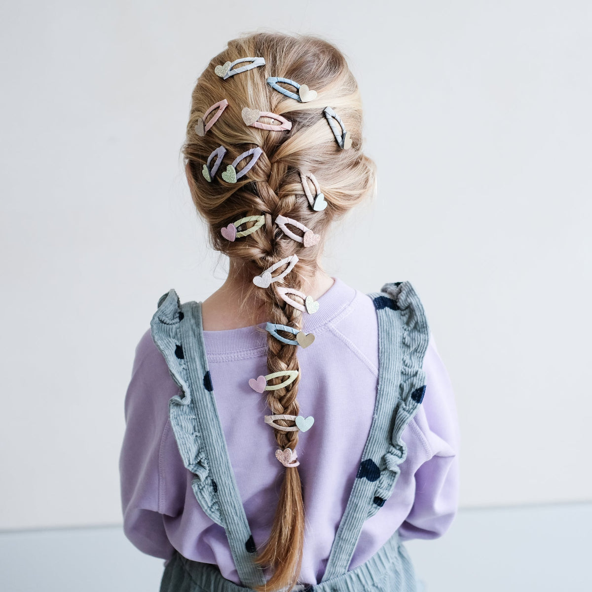 Person with braided hair adorned with colorful hair clips on a plain background