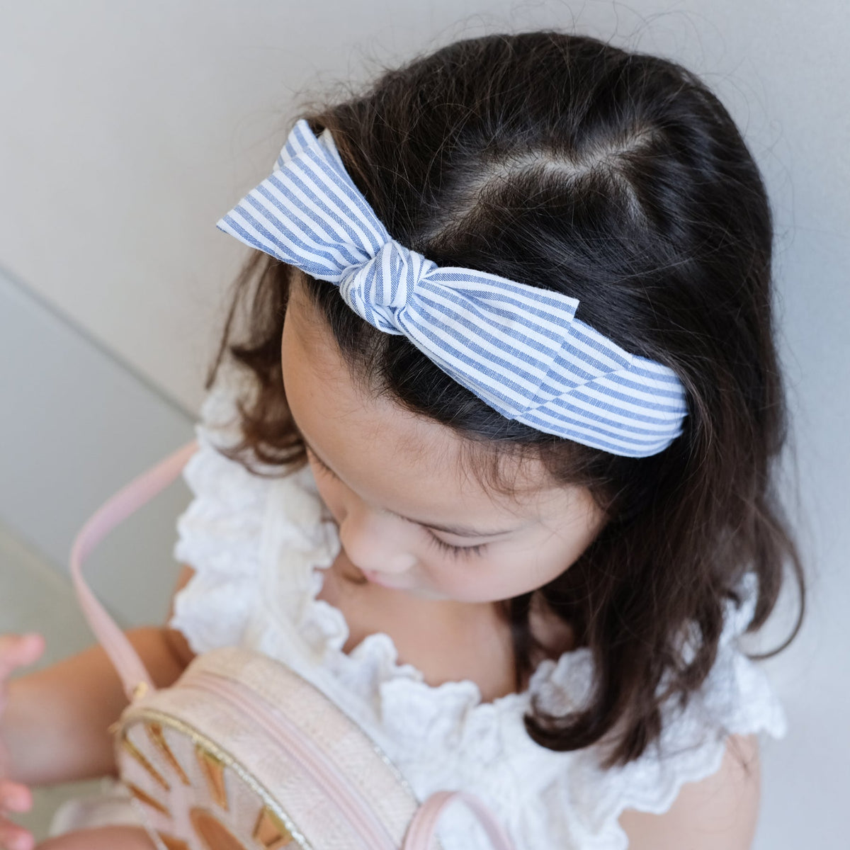 A girl wearing striped headband with a bow on a grey background