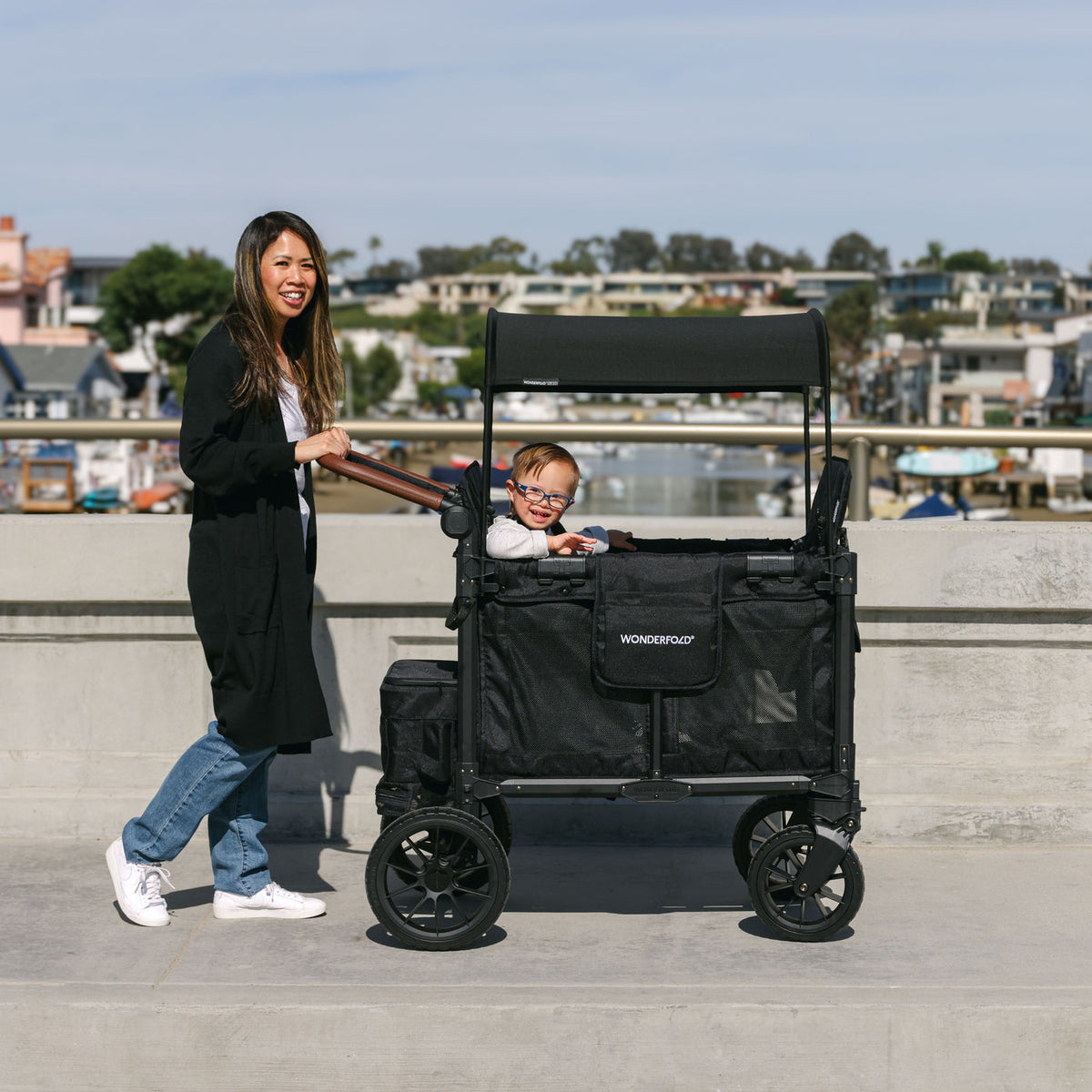 Woman pushing a black wagon with a child inside on a concrete surface.
