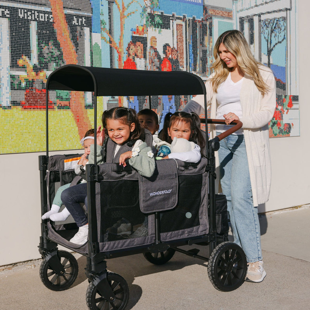 Woman pushing a stroller with children in front of a colorful mural.
