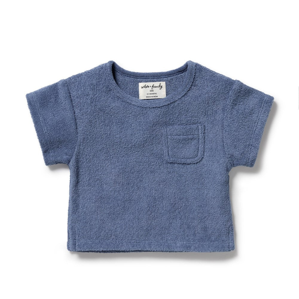 A dusty blue short-sleeve baby t-shirt with a textured terry cloth fabric, featuring a small chest pocket and a white brand label inside the collar, shown on a plain white background.