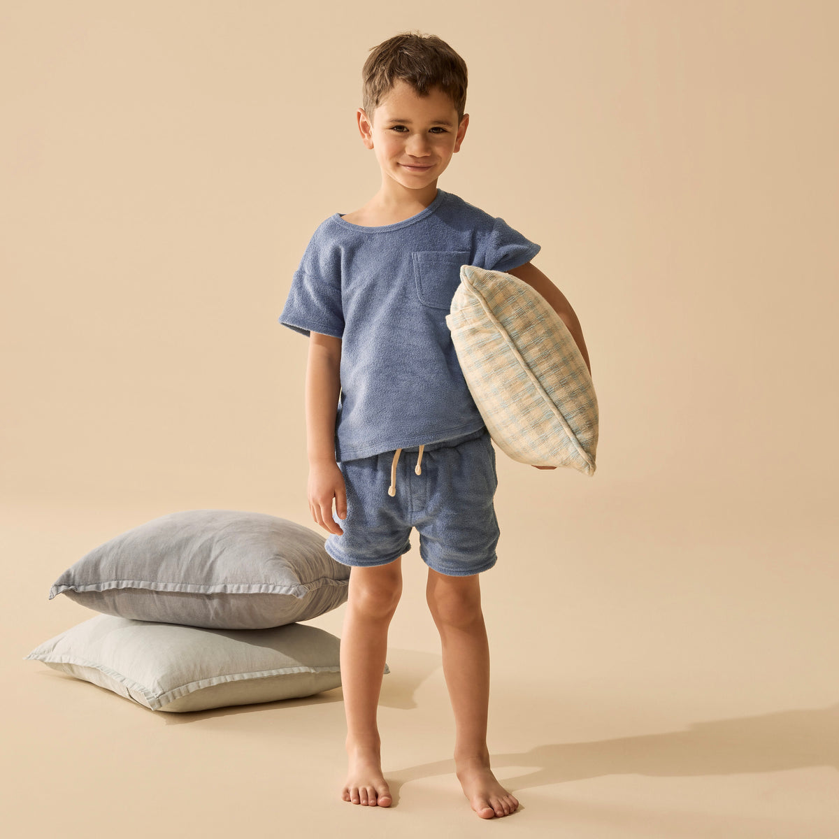 Child holding a pillow with pillows on the floor against a beige background