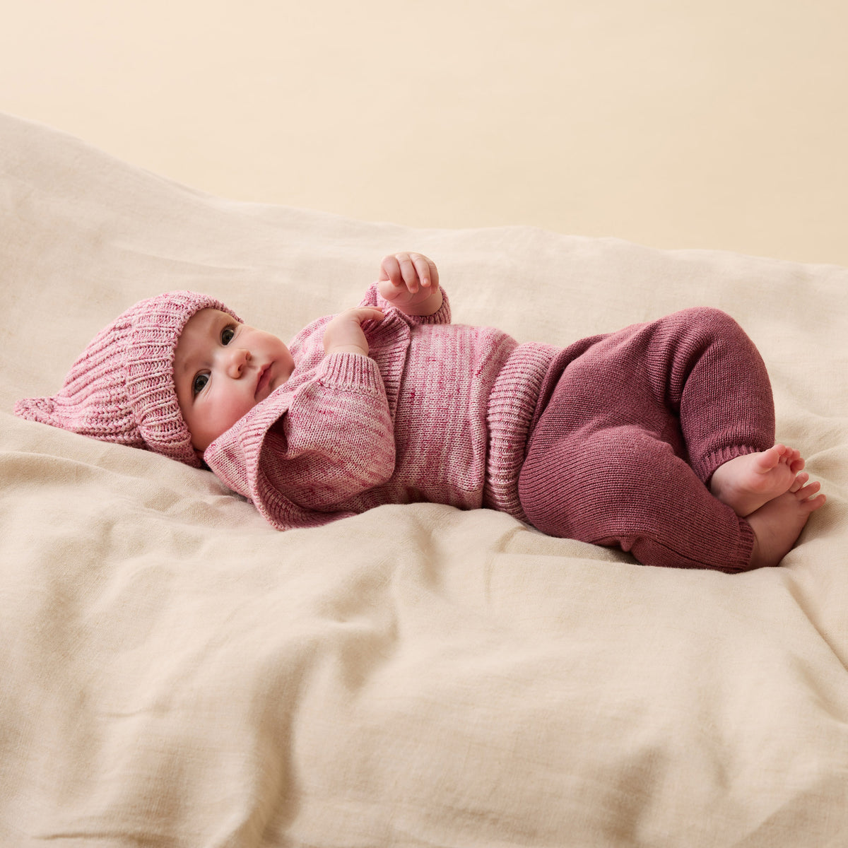 Baby in pink knitted outfit lying on a beige blanket