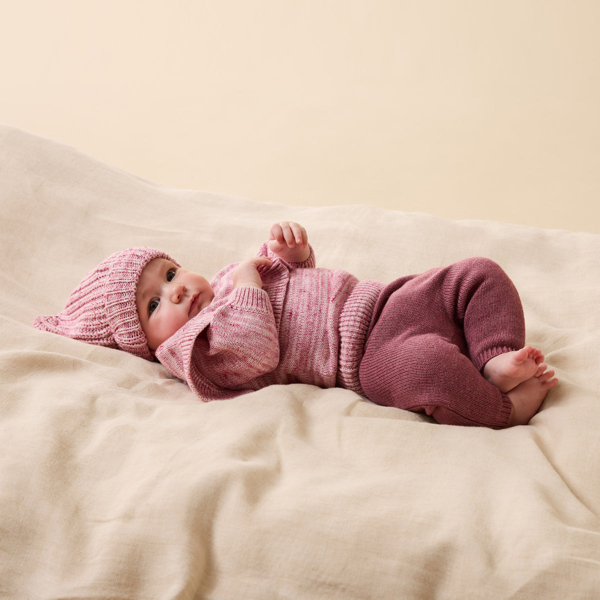 Baby in pink knitted outfit lying on a beige blanket