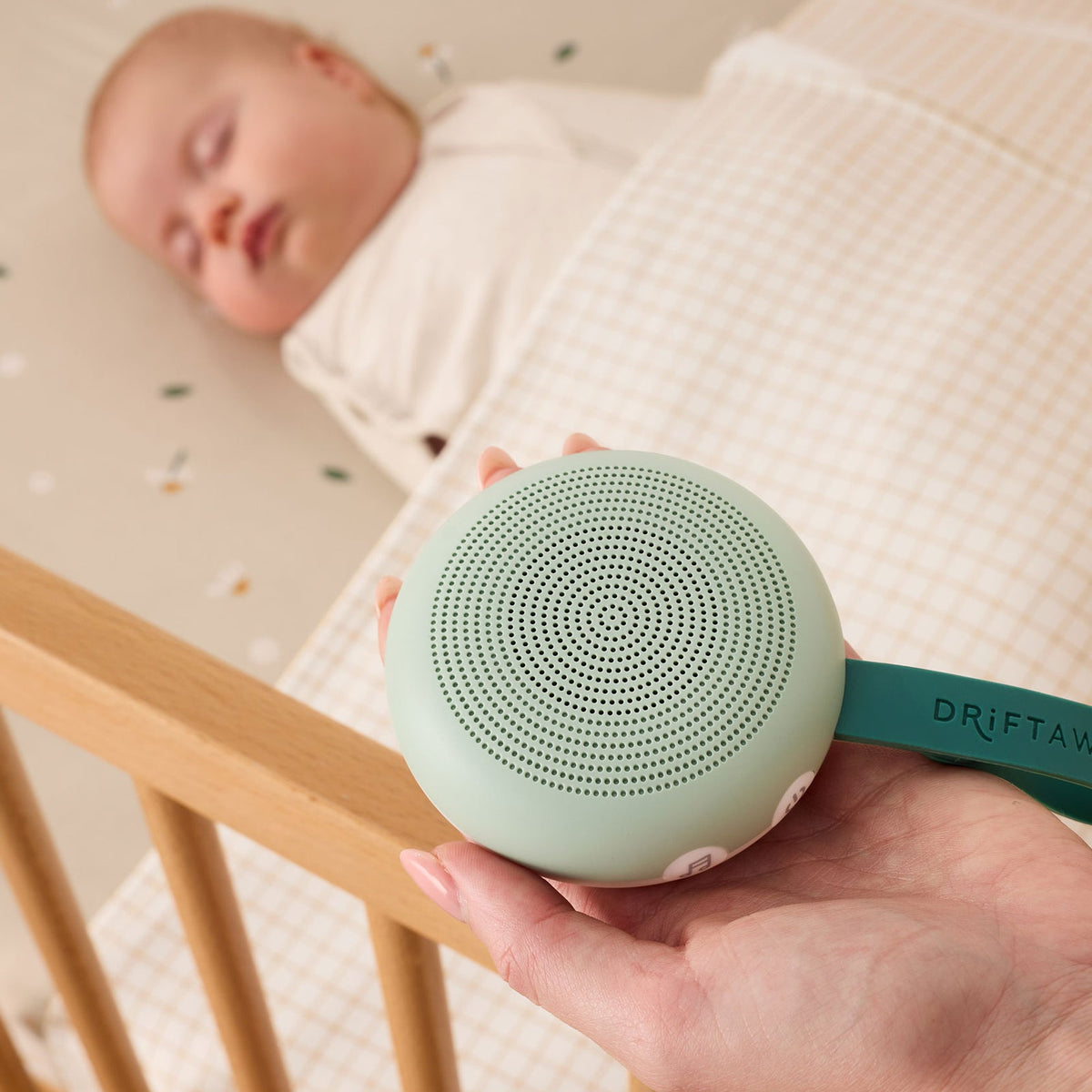 Person holding a green baby monitor device next to a sleeping baby in a crib.