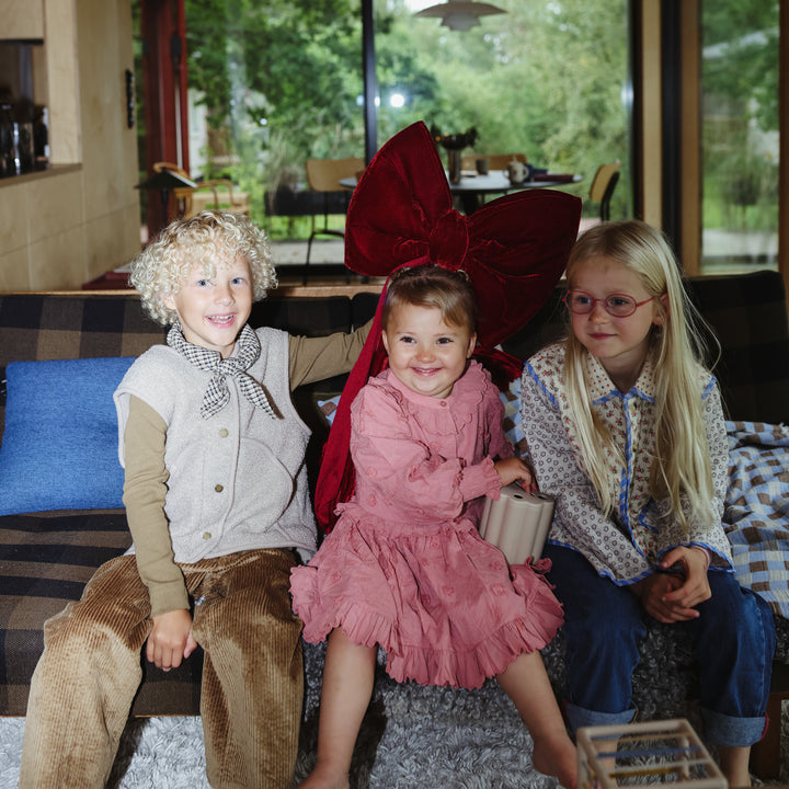Three children sitting on a couch with one wearing a large red bow.