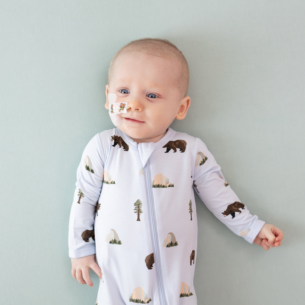 Baby wearing a onesie with bear and mountain patterns against a light gray background