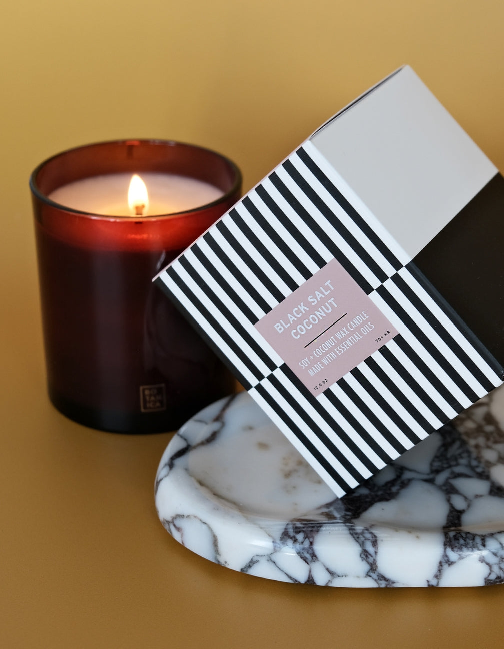 Candle with a striped box on a marble coaster against a yellow background