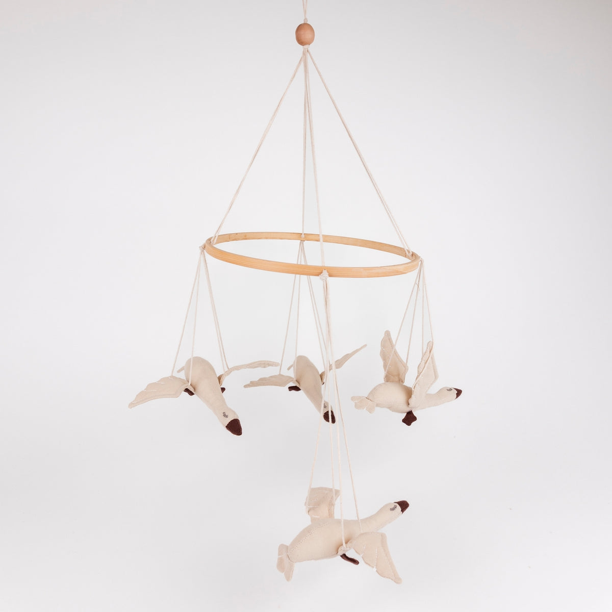 A fabric bird mobile hanging from a light wood ring on a white background. The mobile features four cream-colored birds with dark brown beaks and feet, suspended by thin cream cords from a wooden bead at the top.