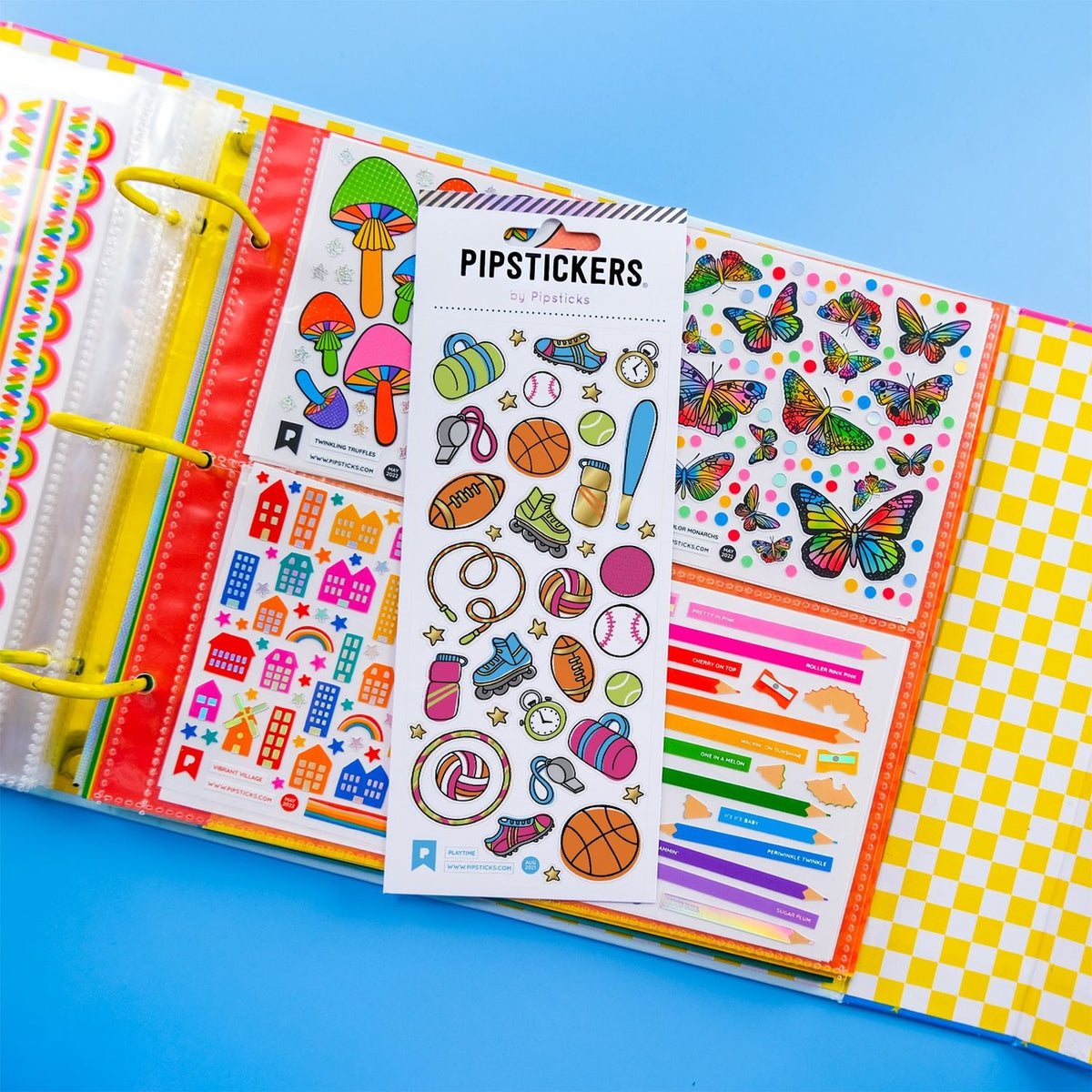 A colorful sticker binder or planner ring set shown open on a bright blue background. The center sheet prominently reads 'PIPSSTICKERS' and features many cartoon-style stickers including mushrooms, sports items, pretzels, volleyballs, and butterflies.