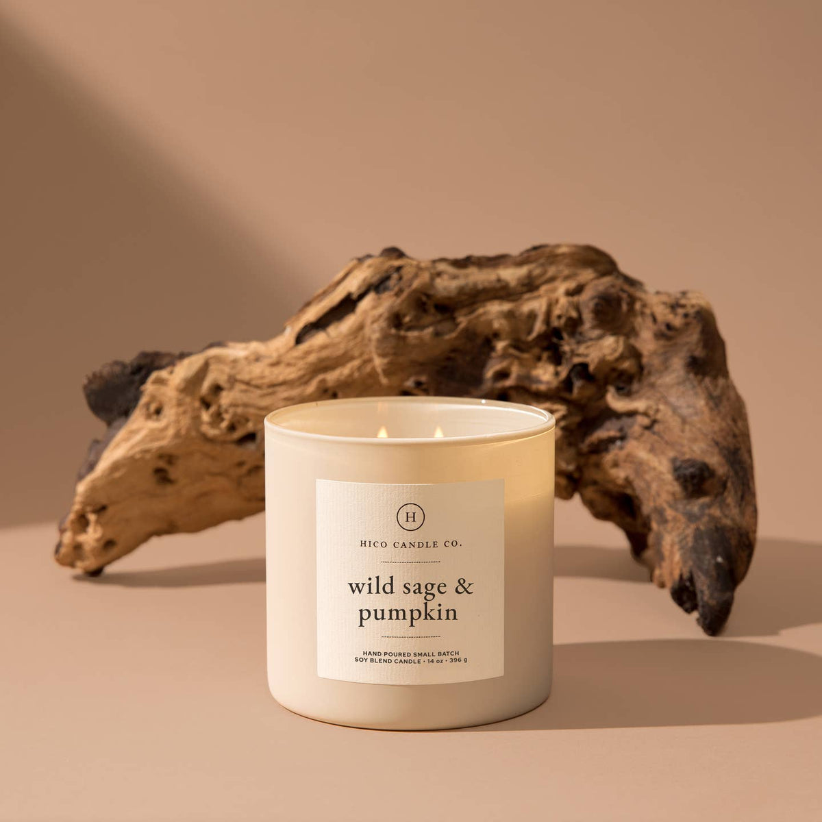 Candle with 'wild sage & pumpkin' label in front of a piece of driftwood on a beige background