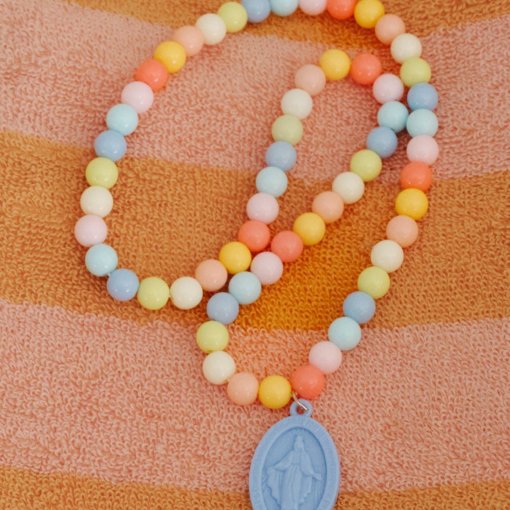 Colorful beaded bracelet with a blue pendant on an orange and pink striped fabric background