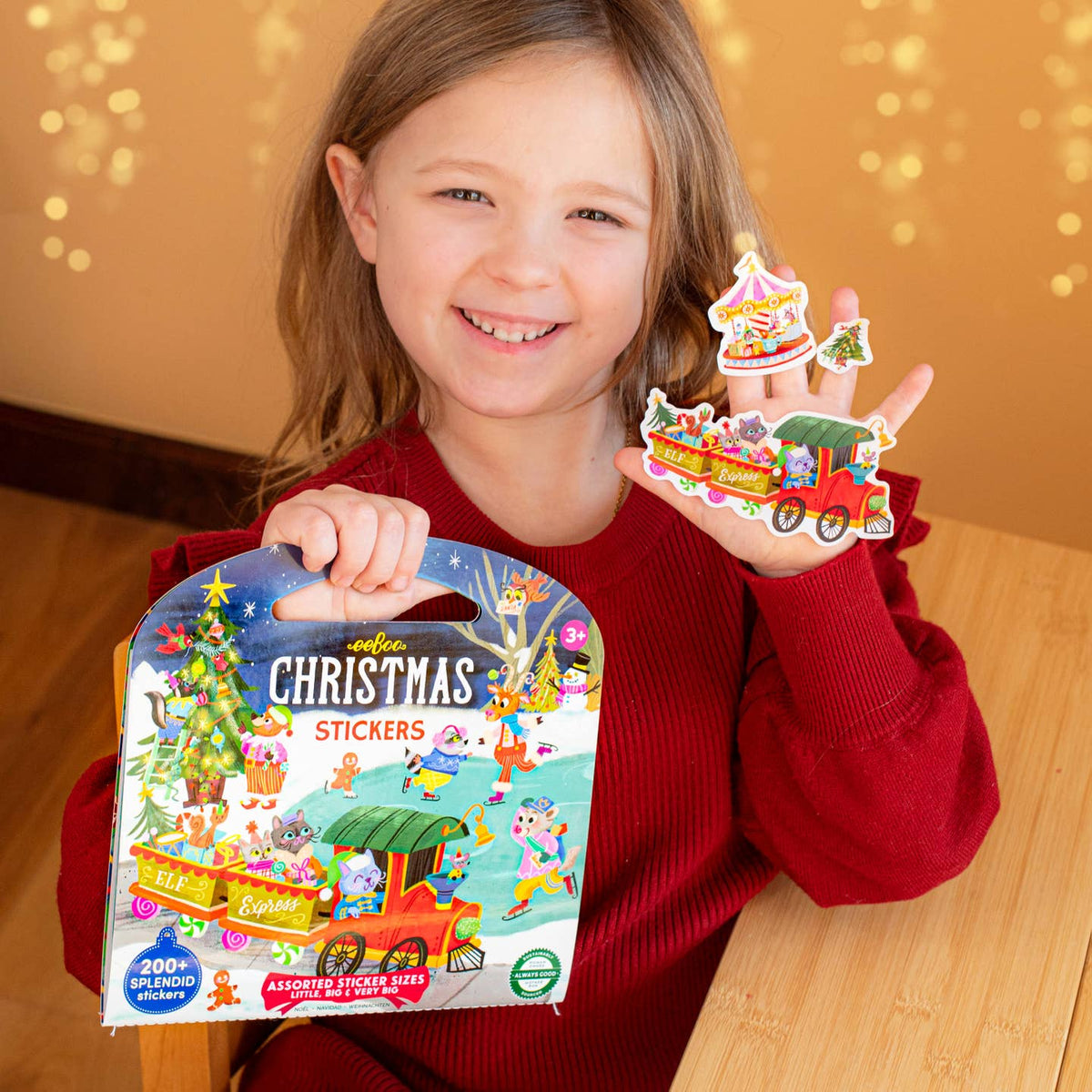 Child holding a box of Christmas stickers and two stickers in front of a warm background