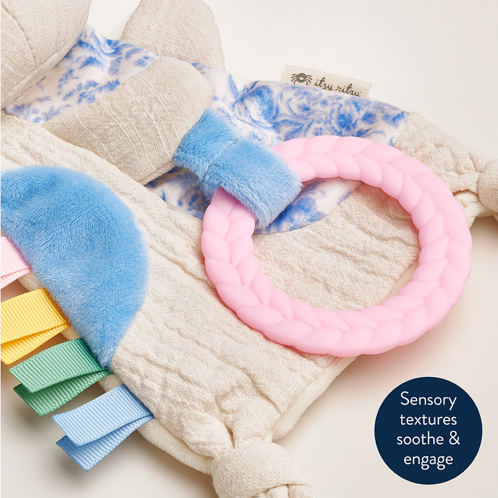 Baby toy with textured elements and a pink ring on a soft fabric background