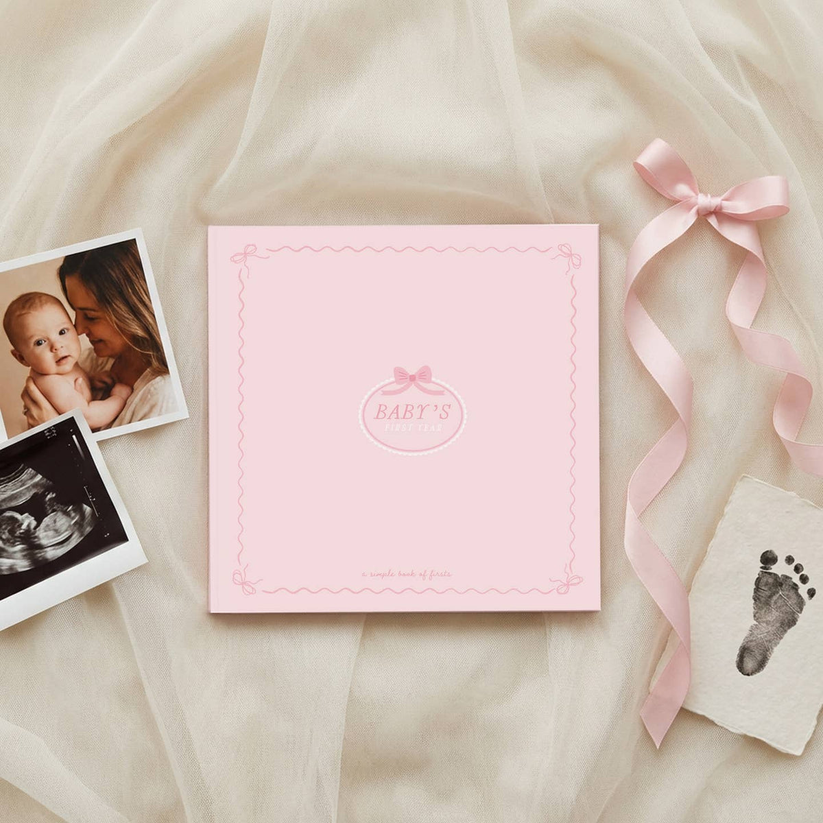 Pink baby album with ultrasound photo, footprint, and ribbon on a soft fabric background