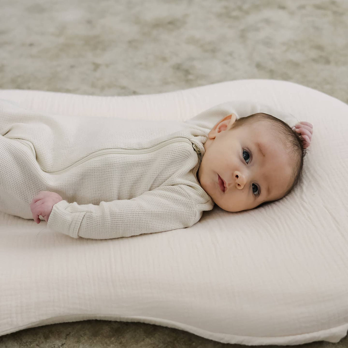 Baby lying on a white cushion with a neutral background