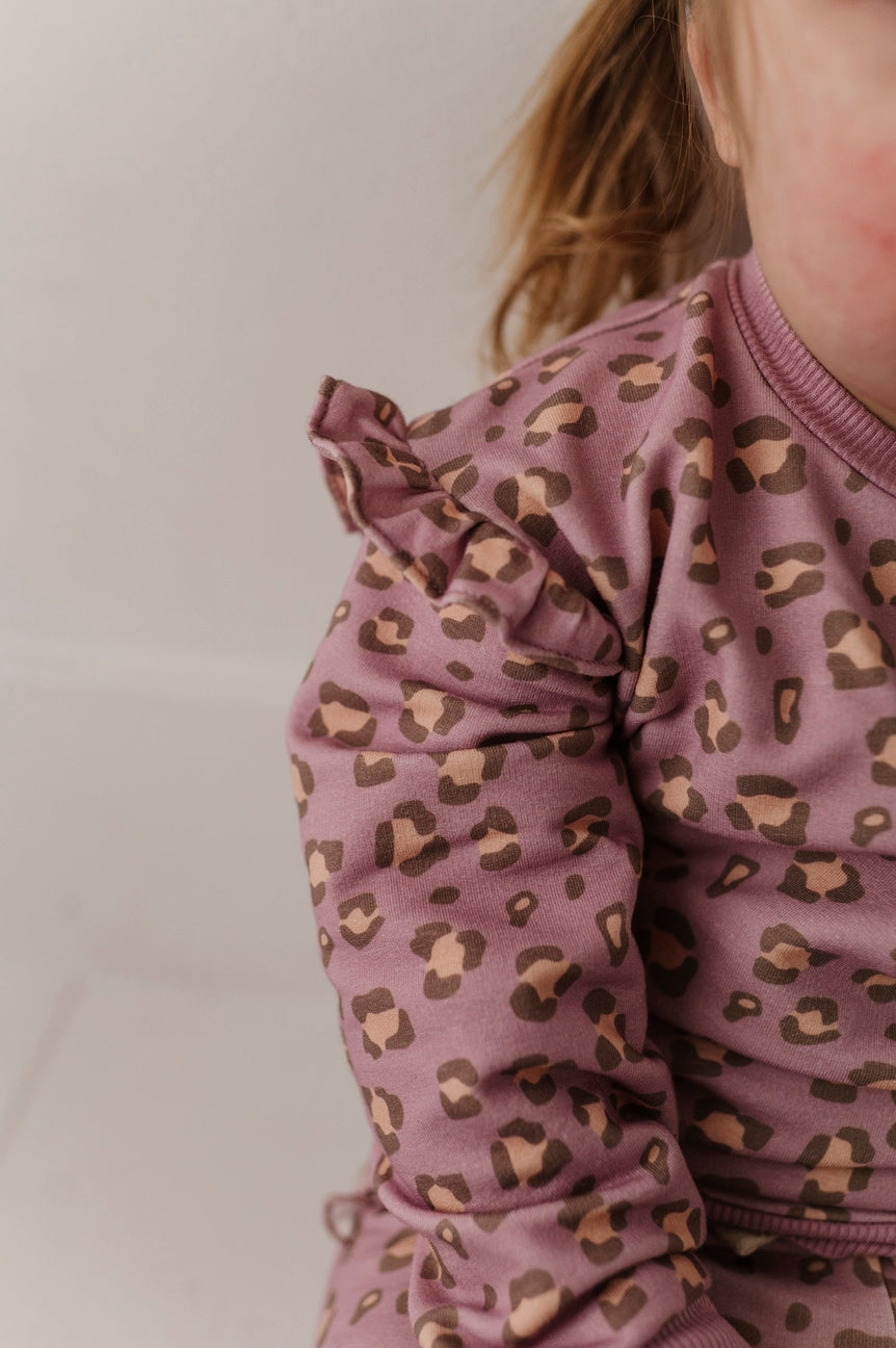Child wearing a pink leopard print outfit against a plain background