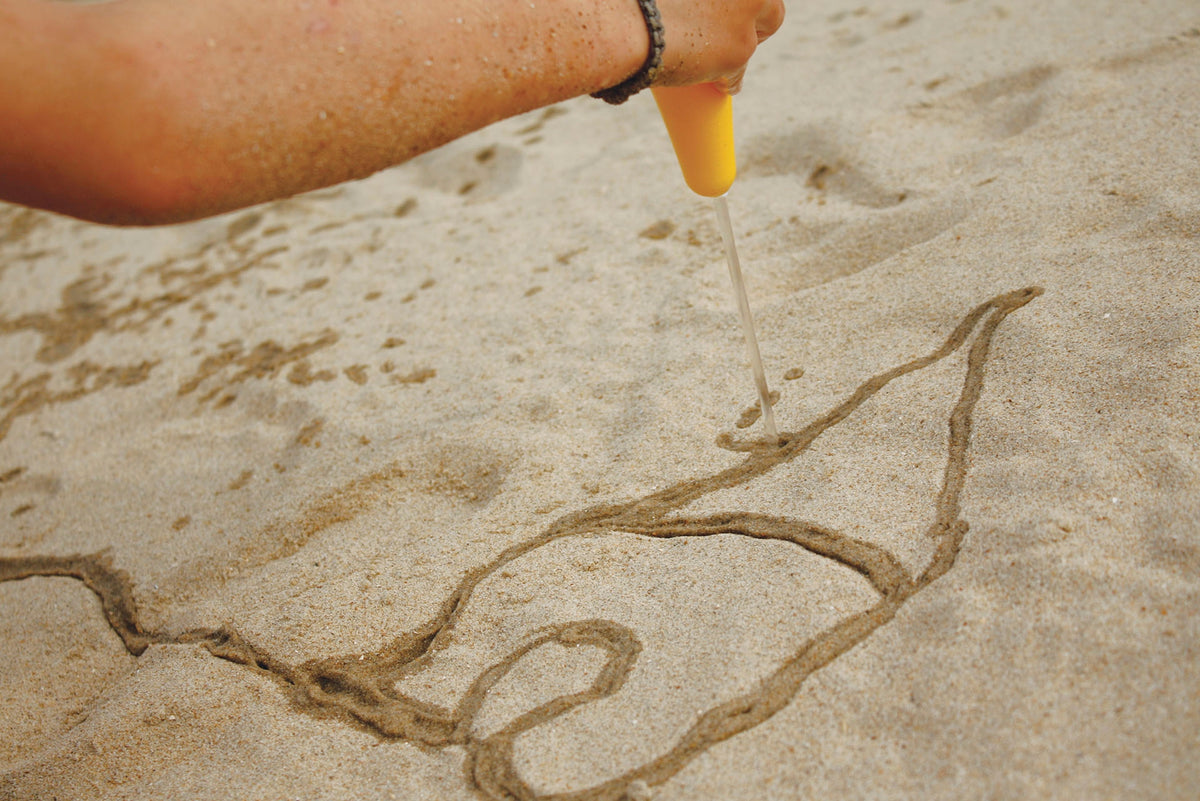 Person drawing a design in sand with a yellow tool