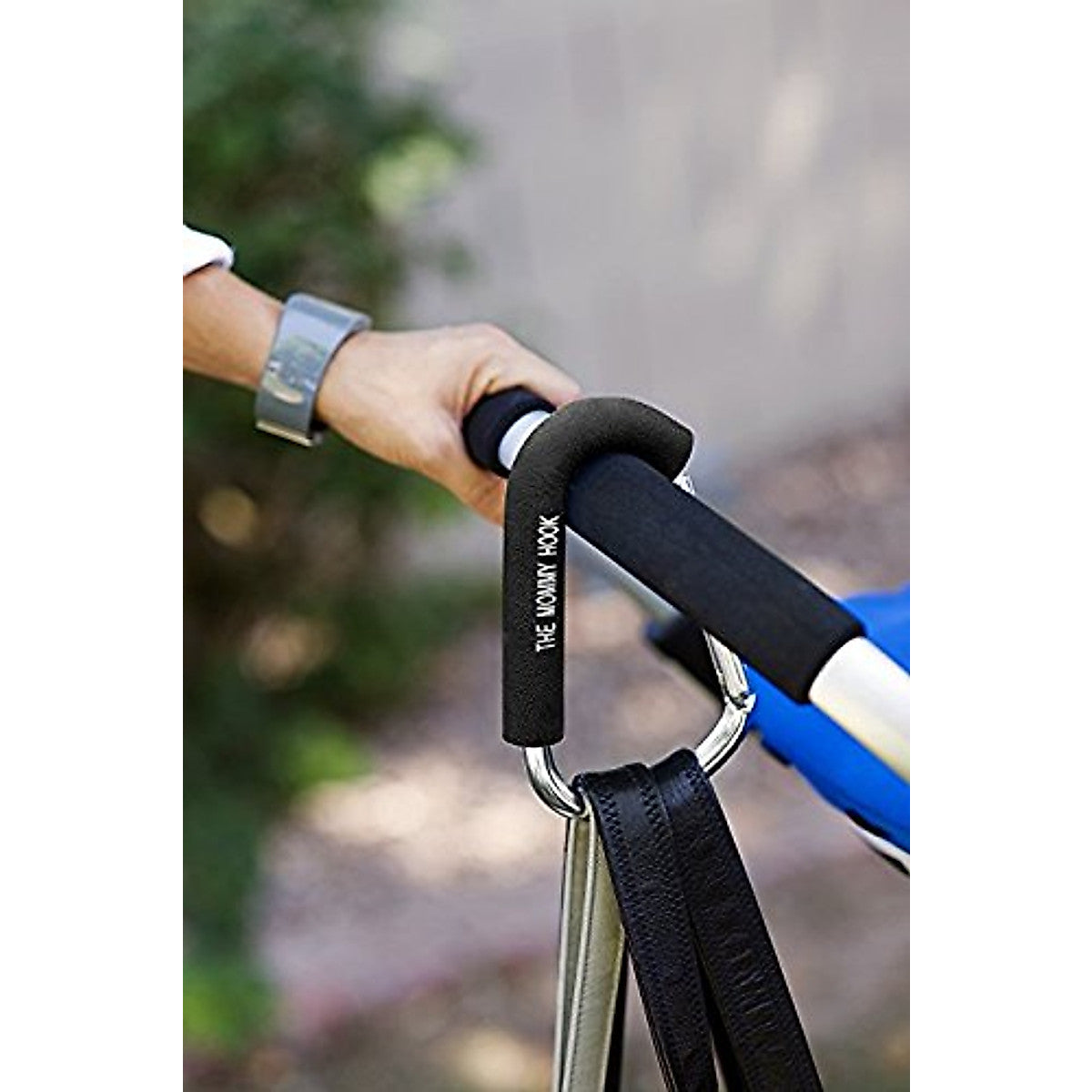 Hand holding a black stroller handle with 'The Mountain' branding, blurred background