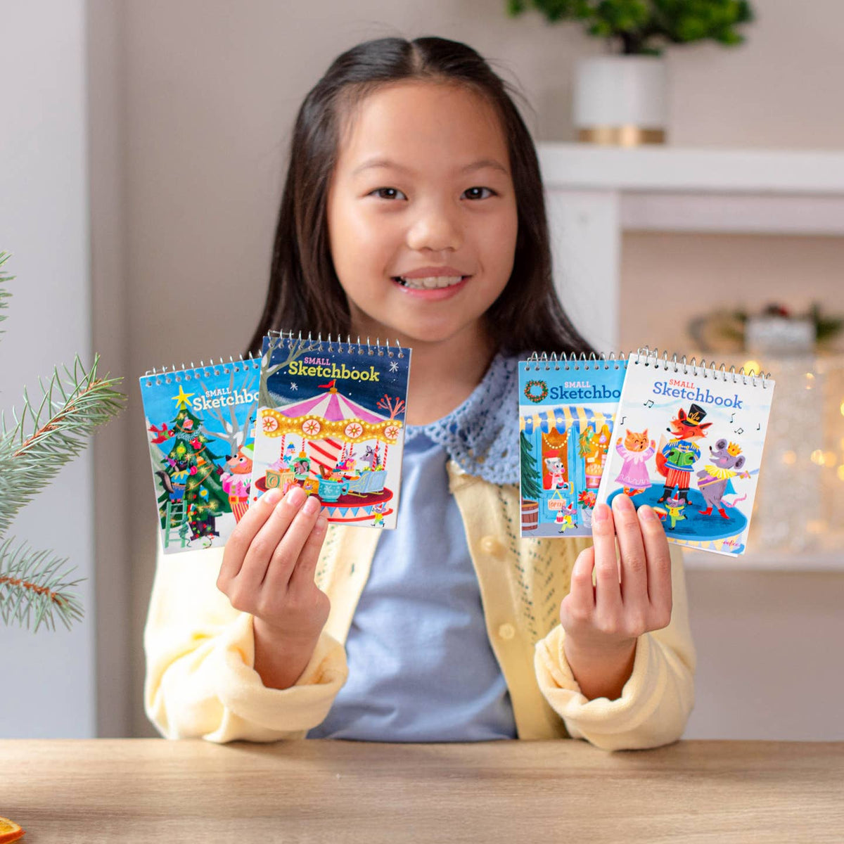Young girl holding colorful sketchbooks with a festive background